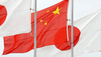 علم الصين واليابان يرفرف بسرعة على سفن الشحن في مرفأ تجاري رئيسي.